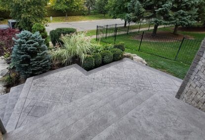 An elevated view of a modern stamped concrete patio and wide steps with a textured gray slate pattern.